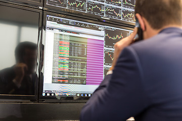 Image showing Stock broker trading online, talking on mobile phone.