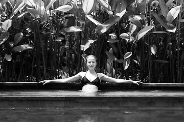 Image showing Sensual young woman relaxing in outdoor spa infinity swimming pool surrounded with lush tropical greenery of Ubud, Bali. Black and white image.