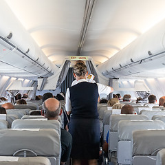 Image showing Interior of commercial airplane with stewardess serving passengers on seats during flight.