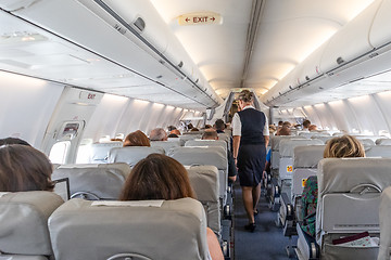 Image showing Interior of commercial airplane with stewardess serving passengers on seats during flight.