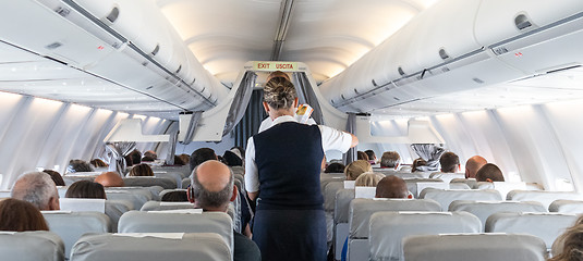 Image showing Interior of commercial airplane with stewardess serving passengers on seats during flight.