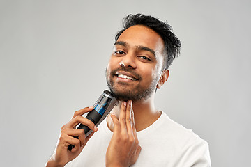 Image showing smiling indian man shaving beard with trimmer