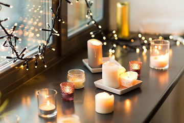 Image showing candles burning on window sill with garland lights