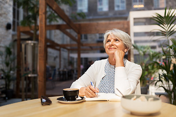 Image showing senior woman with notebook dreaming at street cafe