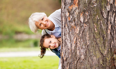 Image showing grandmother and granddaughter behind tree at park