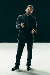 Image showing Male beauty concept. Portrait of a fashionable young man with stylish haircut wearing trendy suit posing over black background.
