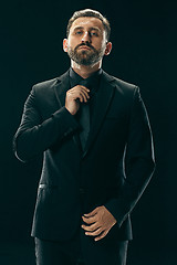 Image showing Male beauty concept. Portrait of a fashionable young man with stylish haircut wearing trendy suit posing over black background.