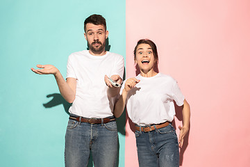 Image showing Closeup portrait of young couple, man, woman. One being excited happy smiling, other serious, concerned, unhappy on pink and blue background. Emotion contrasts