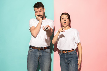 Image showing Closeup portrait of young couple, man, woman. One being excited happy smiling, other serious, concerned, unhappy on pink and blue background. Emotion contrasts