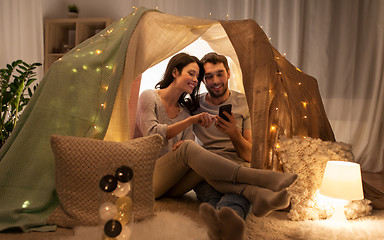 Image showing happy couple with smartphone in kids tent at home