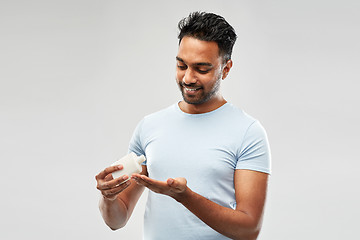 Image showing happy indian man applying lotion to his hand