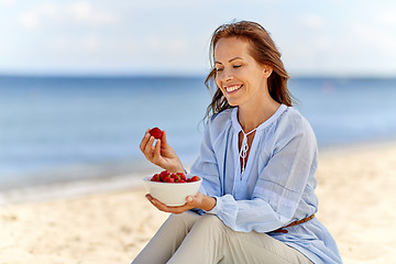 Image showing happy woman eating strawberries on summer beach