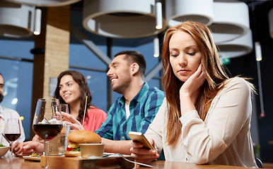 Image showing bored woman messaging on smartphone at restaurant