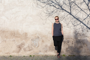 Image showing Graphical and textured artisic image of modern trendy fashionable woman wearing sunglasses leaning against old textured retro wall with tree shadow falling on the wall.