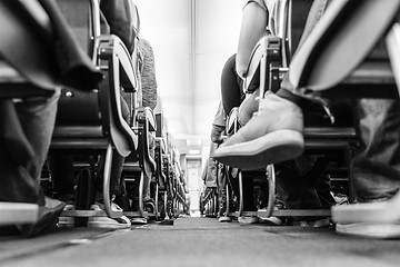 Image showing Low agle view of passenegers commercial airplane aisle with passenegers sitting on their seats while flying. Black and white photo.