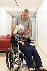 Image showing Middle aged man showing and helping elderly 95 years old woman sitting at the wheelchair how to use modern mobile phone.