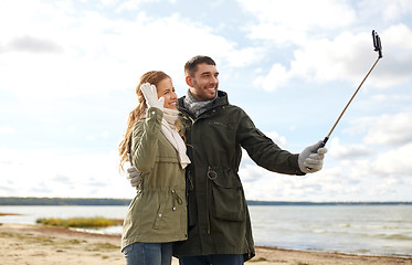 Image showing happy couple taking selfie on beach in autumn