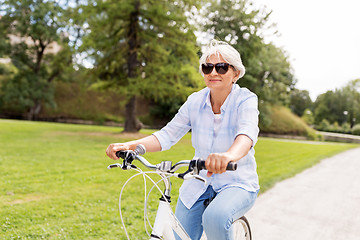 Image showing happy senior woman riding bicycle at summer park