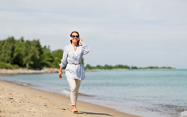 Image showing woman with headphones walking along summer beach