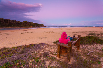 Image showing Woman relaxes on bench overlooking beach in the afternoon dusk