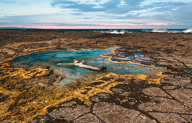 Image showing Female leisurely floating in a rock pool by the ocean