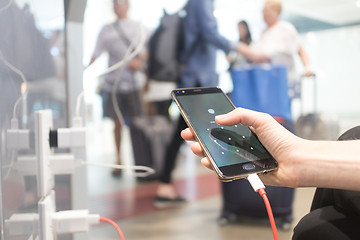 Image showing Female hands holding and using smartphone while charging it in a public place using electric plug and a charging cable