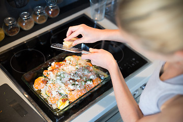 Image showing Female chef grinding parmesan cheese on row vegetarian dish ingredients in glass baking try before placing it into oven. Healthy home-cooked everyday vegetarian food