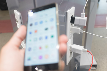 Image showing Female hands holding cell phone and using smartphone apps while charging it in a public place using electric plug and a charging cable. Focus on charging adapter.