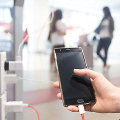 Image showing Female hands holding and using smartphone while charging it in a public place using electric plug and a charging cable