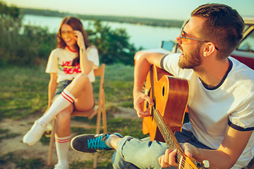 Image showing Couple sitting and resting on the beach playing guitar on a summer day near river