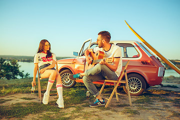 Image showing Couple sitting and resting on the beach playing guitar on a summer day near river