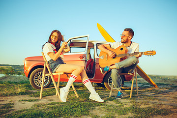 Image showing Couple sitting and resting on the beach playing guitar on a summer day near river