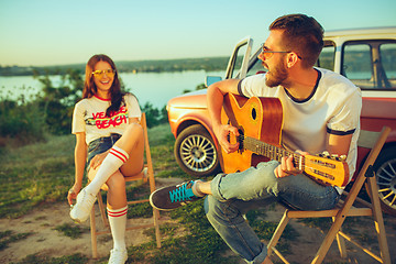 Image showing Couple sitting and resting on the beach playing guitar on a summer day near river