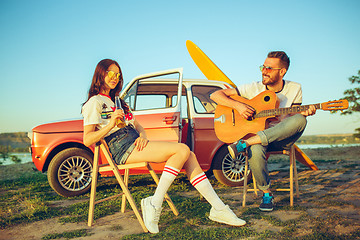Image showing Couple sitting and resting on the beach playing guitar on a summer day near river