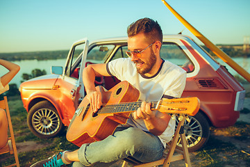 Image showing Couple sitting and resting on the beach playing guitar on a summer day near river