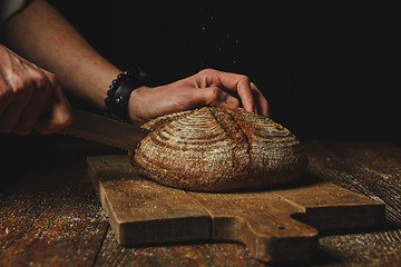 Image showing Hands of a young man cut fresh rye bread