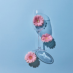 Image showing Three pink flowers gerbera and a glass on a blue background