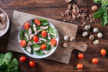 Image showing A plate of salad from boiled meat, quail eggs, spinach and tomatoes on a wooden board on the kitchen table. Dietary snack Flat lay