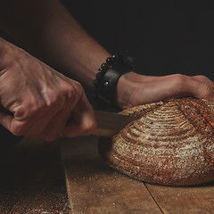 Image showing man cuts a round dark bread