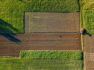 Image showing Aerial view from the drone, a bird\'s eye view of agricultural fields with a road through and a tractor on it in the spring evening at sunset