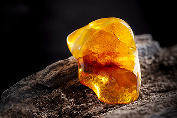 Image showing Natural amber. A piece of yellow opaque natural amber on large piece of dark stoned wood.