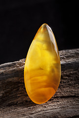 Image showing Natural amber. A piece of yellow opaque natural amber on large piece of dark stoned wood.