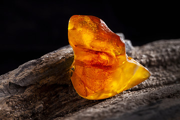 Image showing Natural amber. A piece of yellow and red semi transparent natural amber on piece of stoned wood.