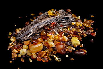 Image showing Natural amber. Many pieces of different colors of natural amber on large piece of stoned wood.