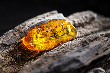 Image showing Natural amber. A piece of yellow transparent natural amber on large piece of dark stoned wood.