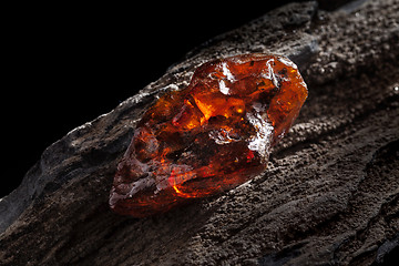 Image showing Natural amber. A piece of yellow and red semi transparent natural amber on piece of stoned wood.