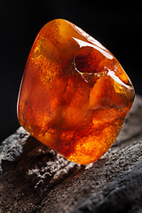 Image showing Natural amber. A piece of yellow and red semi transparent natural amber on piece of stoned wood.