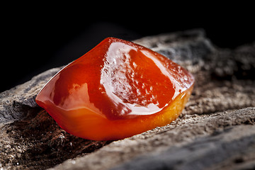 Image showing Natural amber. A piece of yellow and red semi transparent natural amber on piece of stoned wood.