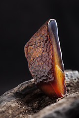 Image showing Natural amber. A piece of dark red semi transparent natural amber on piece of stoned wood.