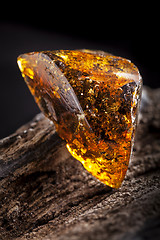 Image showing Natural amber stone. A piece of dirty transparent yellow amber on piece of stoned wood.